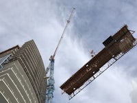 a crane lifts a beam over a tall building